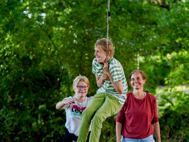 3 Kinder im Garten, eins davon hält sich am Seil fest