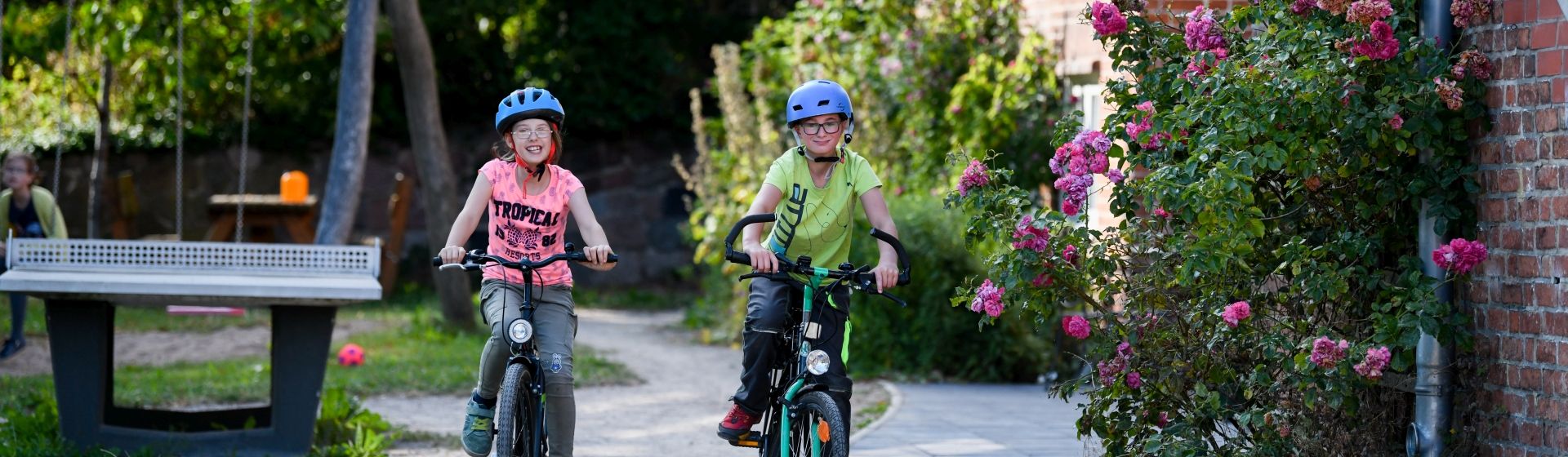 Zwei Kinder fahren auf Fahrrädern an einem Haus vorbei