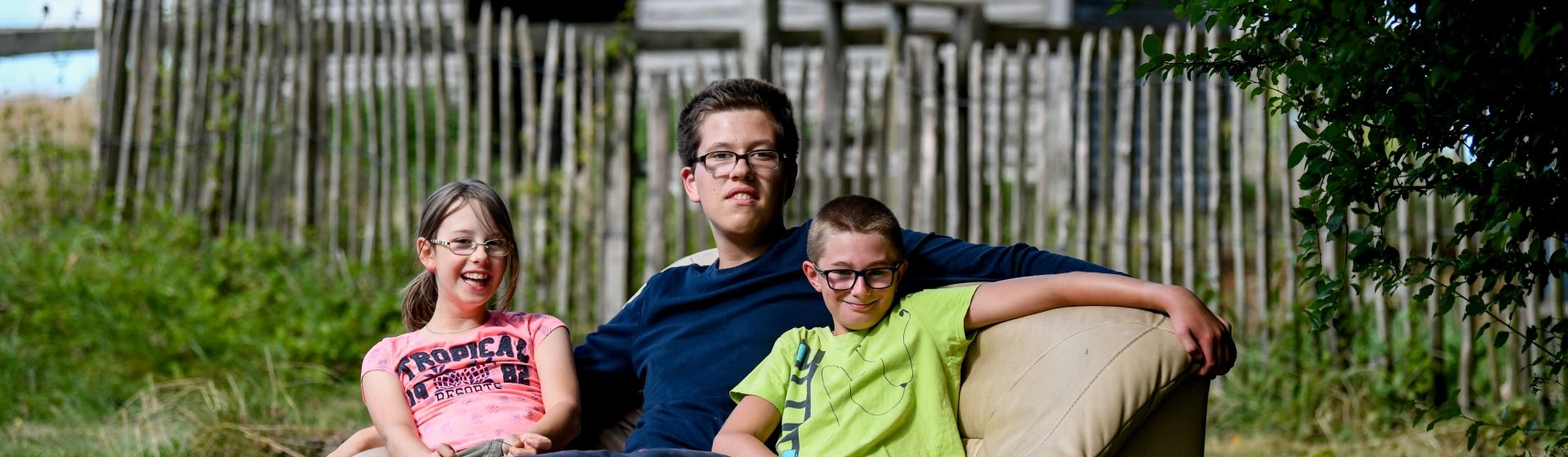 3 Kinder sitzen auf einem Sofa im Garten