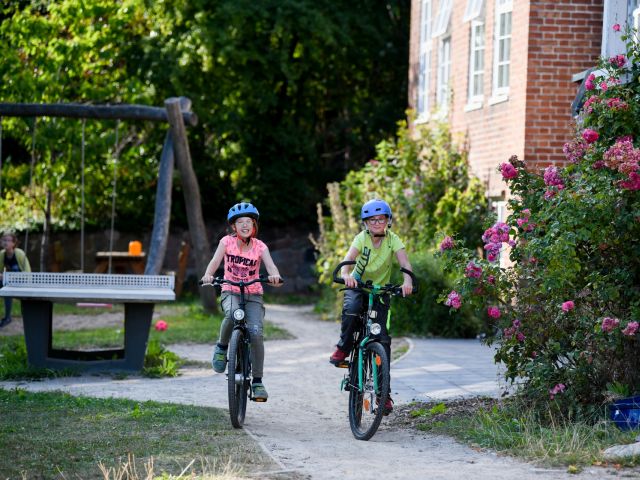 Zwei Kinder fahren auf Fahrrädern an einem Haus vorbei